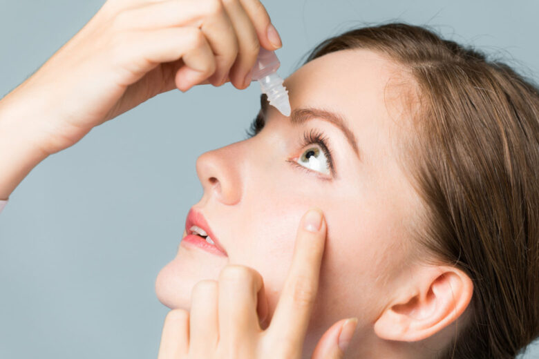 Young woman applying eye lotion.